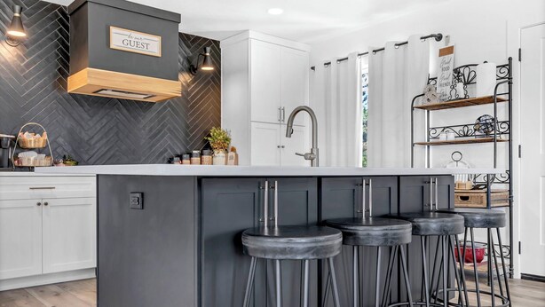 A modern kitchen with a central island, bar stools, a built-in oven, and a herringbone-patterned backsplash. - Large Home In Haysville! (Haysville)