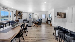 A spacious living area with a wooden dining table, multiple seating options, and a kitchen area with a white countertop and bar stools. - Large Home In Haysville! (Haysville)
