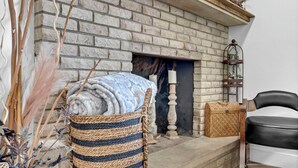 A room with a stone fireplace, a woven basket, a black leather chair, and a wooden chest. - Large Home In Haysville! (Haysville)