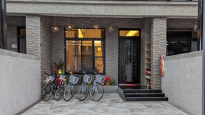 En moderne bygningseingang med cykler parkeret udenfor, en glasdør og et lille udendørs opholdsområde med planter.