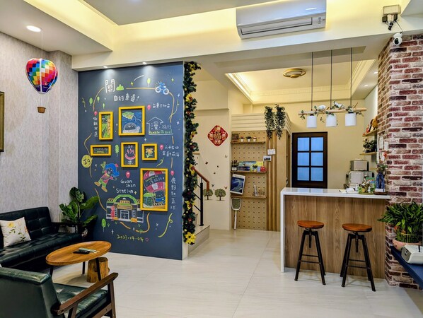 A modern hotel lobby with a large chalkboard wall displaying travel-themed drawings and text, a black leather sofa, wooden stools, and a brick accent wall.