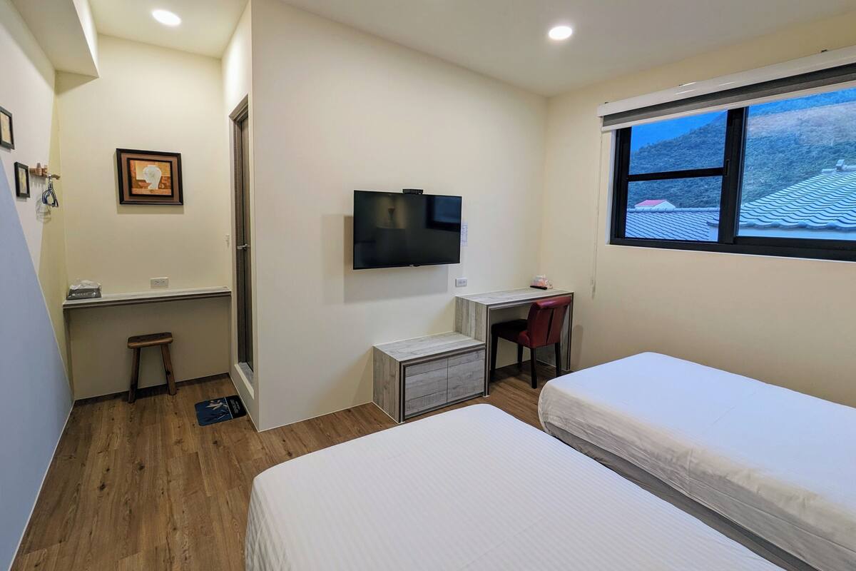 A bedroom with a bed, a desk, a chair, a TV, and a window with a view.