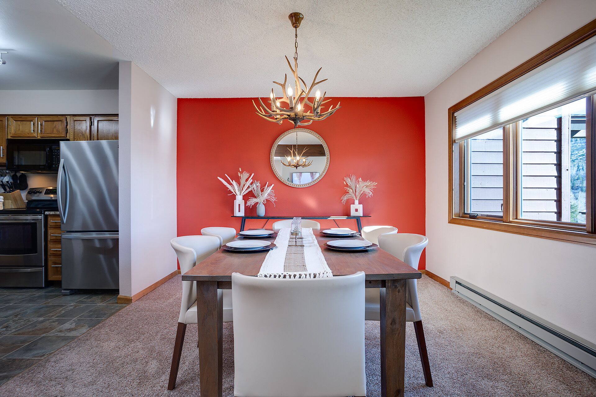 A dining area with a red accent wall, a chandelier, and a large window.