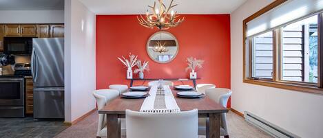 A dining area with a red accent wall, a chandelier, and a large window.