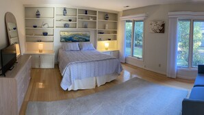 A bedroom with a bed, a sofa, a large window, and built-in shelves with decorative items. - Harbour Town Golf Links 11th Tee Ranch Walkable to Harbour Town (Hilton Head Island)