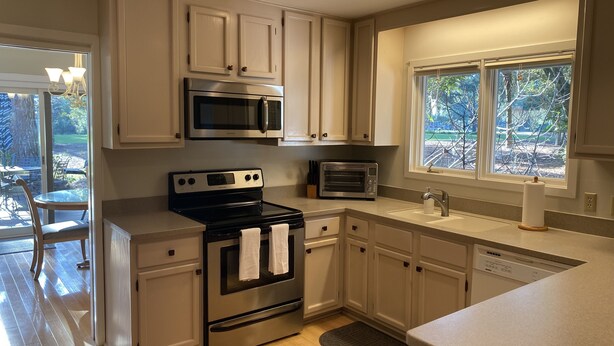 A modern kitchen with stainless steel appliances, white cabinetry, and a large window providing natural light. - Harbour Town Golf Links 11th Tee Ranch Walkable to Harbour Town (Hilton Head Island)
