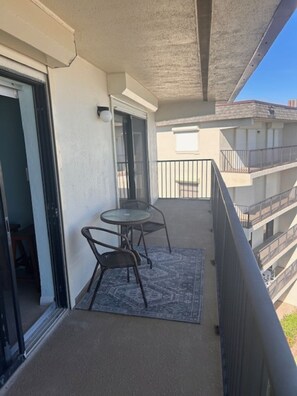 A balcony with a glass door, a small round table with chairs, and a patterned rug. - TOP FLOOR Spectacular Ocean and Pool View Condo  (Ormond Beach)