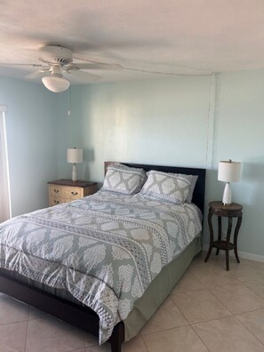 A bedroom with a bed, two bedside tables, a ceiling fan, and a window. - TOP FLOOR Spectacular Ocean and Pool View Condo  (Ormond Beach)