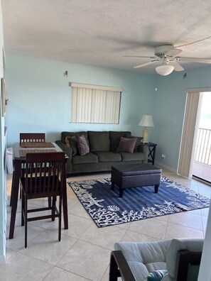 A living room with a dining area, a ceiling fan, and a large window with blinds. - TOP FLOOR Spectacular Ocean and Pool View Condo  (Ormond Beach)