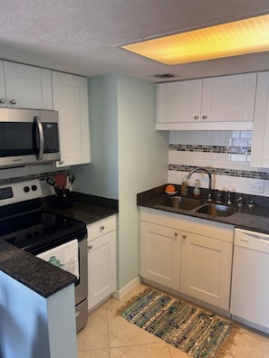 A compact kitchen with white cabinets, a microwave, stove, and sink. - TOP FLOOR Spectacular Ocean and Pool View Condo  (Ormond Beach)