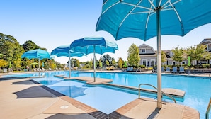 Una piscina con numerosi ombrelloni blu, poltrone prendisole e un cielo azzurro.