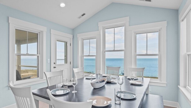 Comedor con vista al mar, sillas blancas, una mesa oscura y un frutero.