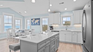 Una cocina moderna con armarios blancos, una isla grande y vista al mar.