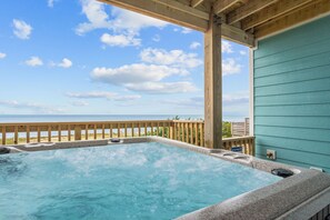 Un jacuzzi avec vue sur l’océan, une terrasse en bois et un bâtiment aux couleurs turquoise.