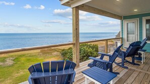 Terraza de madera con sillas Adirondack y una mesa con vistas a la playa y al océano.
