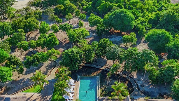 Vista aérea de un resort con piscina, edificios de techo de paja y una playa.