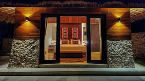 Un edificio de madera con techo de paja, pared de piedra y una cama con ropa de cama estampada.