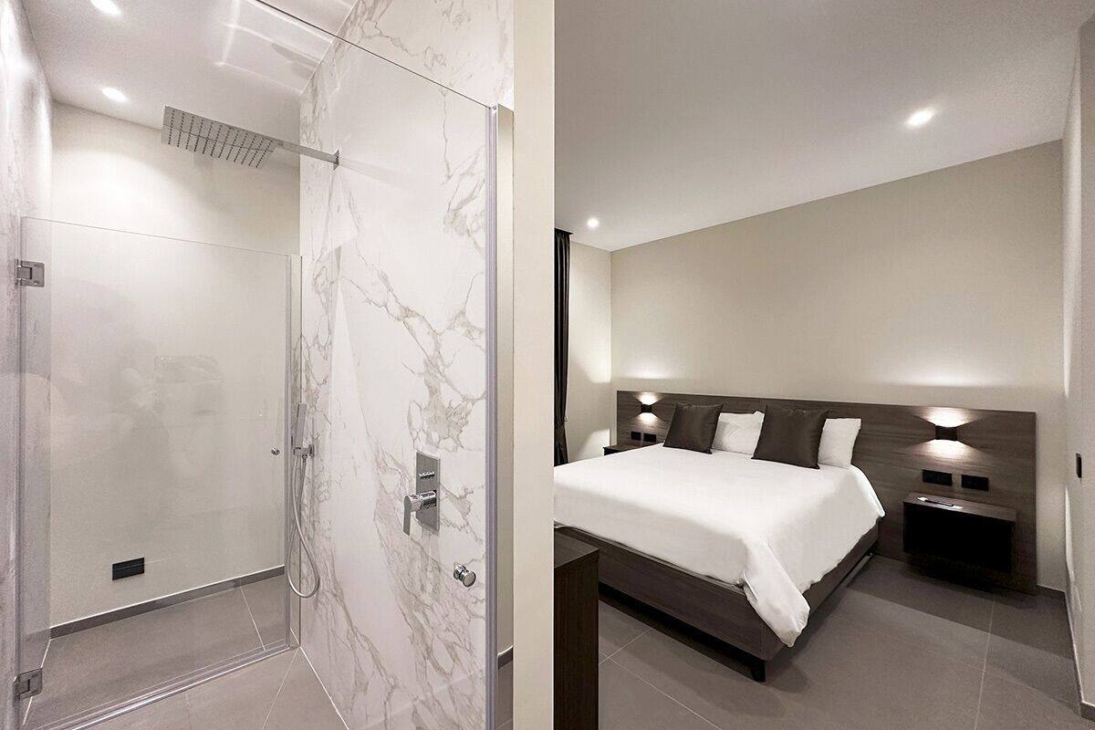A modern bathroom with a glass-enclosed shower and a separate bedroom with a large bed and bedside tables.
