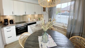 A modern kitchen with white cabinets, a dining table with a vase of dried flowers, and a unique hanging light fixture.