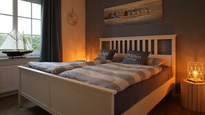 A bedroom with a bed, a window with curtains, a wall clock, a painting, and a ship model.