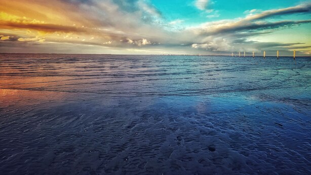 A beach with a view of the ocean and distant wind turbines.