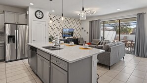 A modern kitchen with a central island, stainless steel appliances, and a dining area with a sofa and table. - Family Oasis: Private Pool, BBQ, Xbox & Disney Nearby! (Kissimmee)