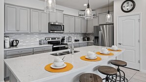 A modern kitchen with white cabinets, stainless steel appliances, and pendant lighting. - Family Oasis: Private Pool, BBQ, Xbox & Disney Nearby! (Kissimmee)