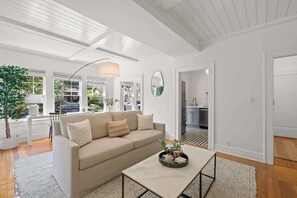A modern living room with a beige sofa, a coffee table with decorative items, and a large window offering a view of the outdoors.