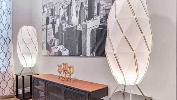 Et moderne interiør med et sort metal konsolbord, en hvid geometrisk lampe og et bybillede på væggen.