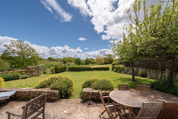 A garden with a stone wall, a wooden table, and chairs.
