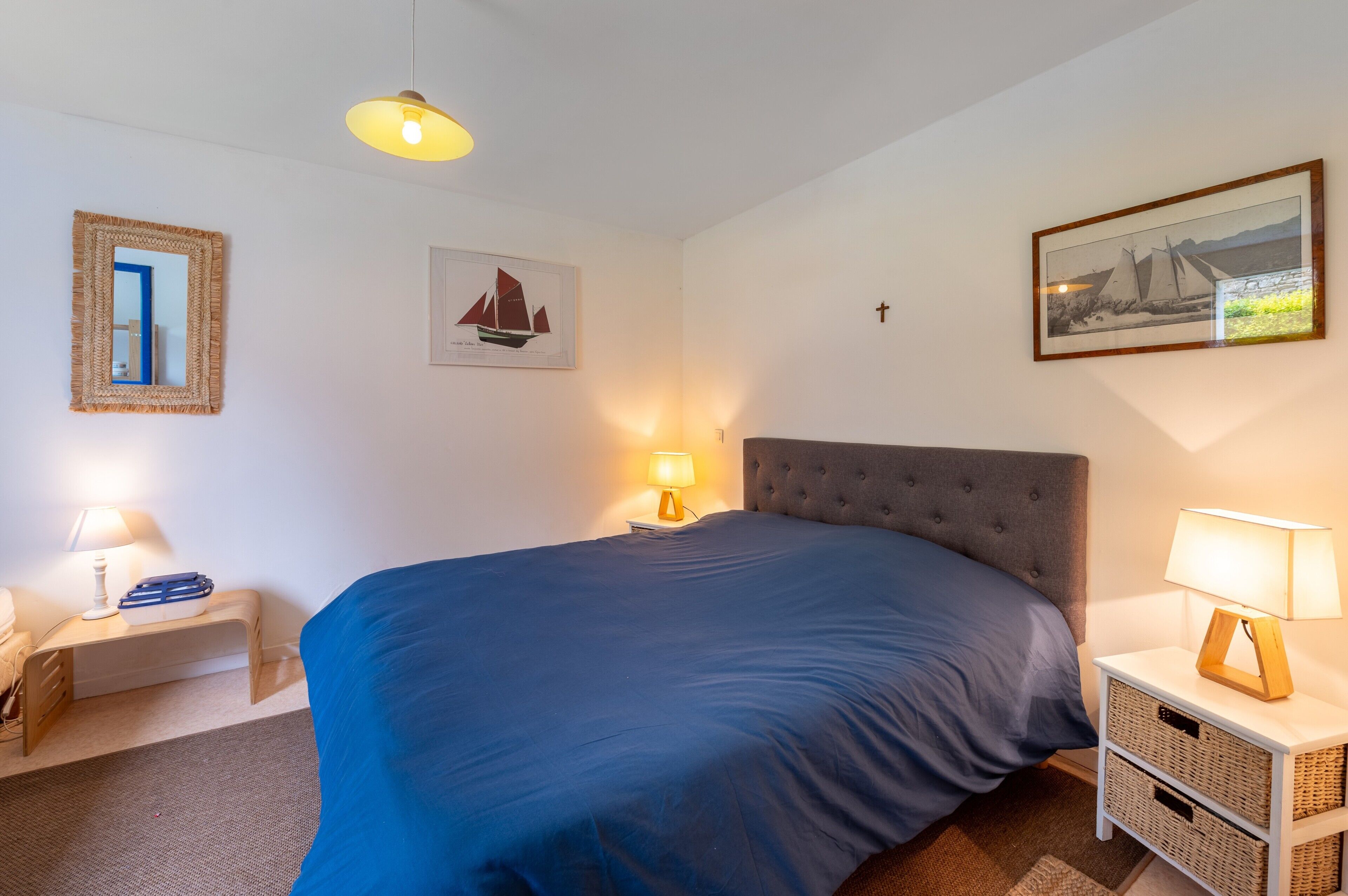Une chambre à coucher comprenant un lit, des lampes de chevet, un miroir fixé au mur et des œuvres d’art encadrées.