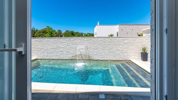 Une piscine avec un mur en pierre et un bâtiment blanc en arrière-plan.