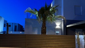 Un bâtiment moderne, avec un palmier devant, un banc en bois et un ciel bleu dégagé.