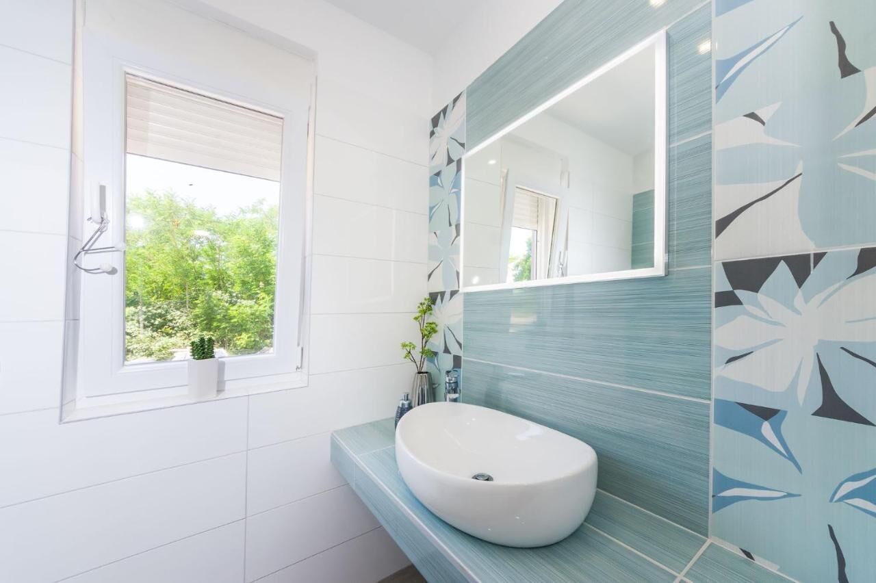A modern bathroom with a large window, a white sink, and a mirror.