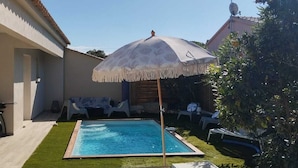 Un giardino sul retro con una piscina, tre poltrone da relax e un ombrellone grande.