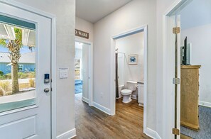 Un couloir menant à une salle de bain équipée de toilettes, d’une douche et d’un meuble en bois.