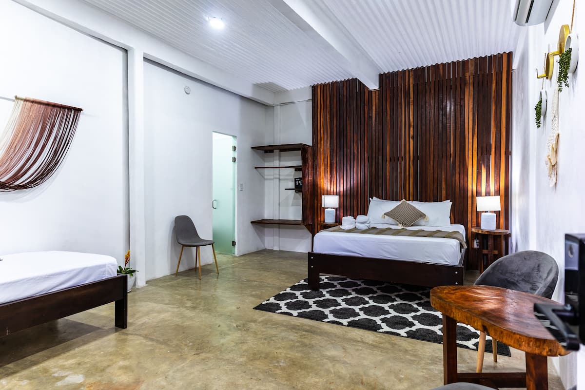 A modern bedroom with a large bed, a desk, and a chair. There is a wooden panel wall and a ceiling with recessed lighting.