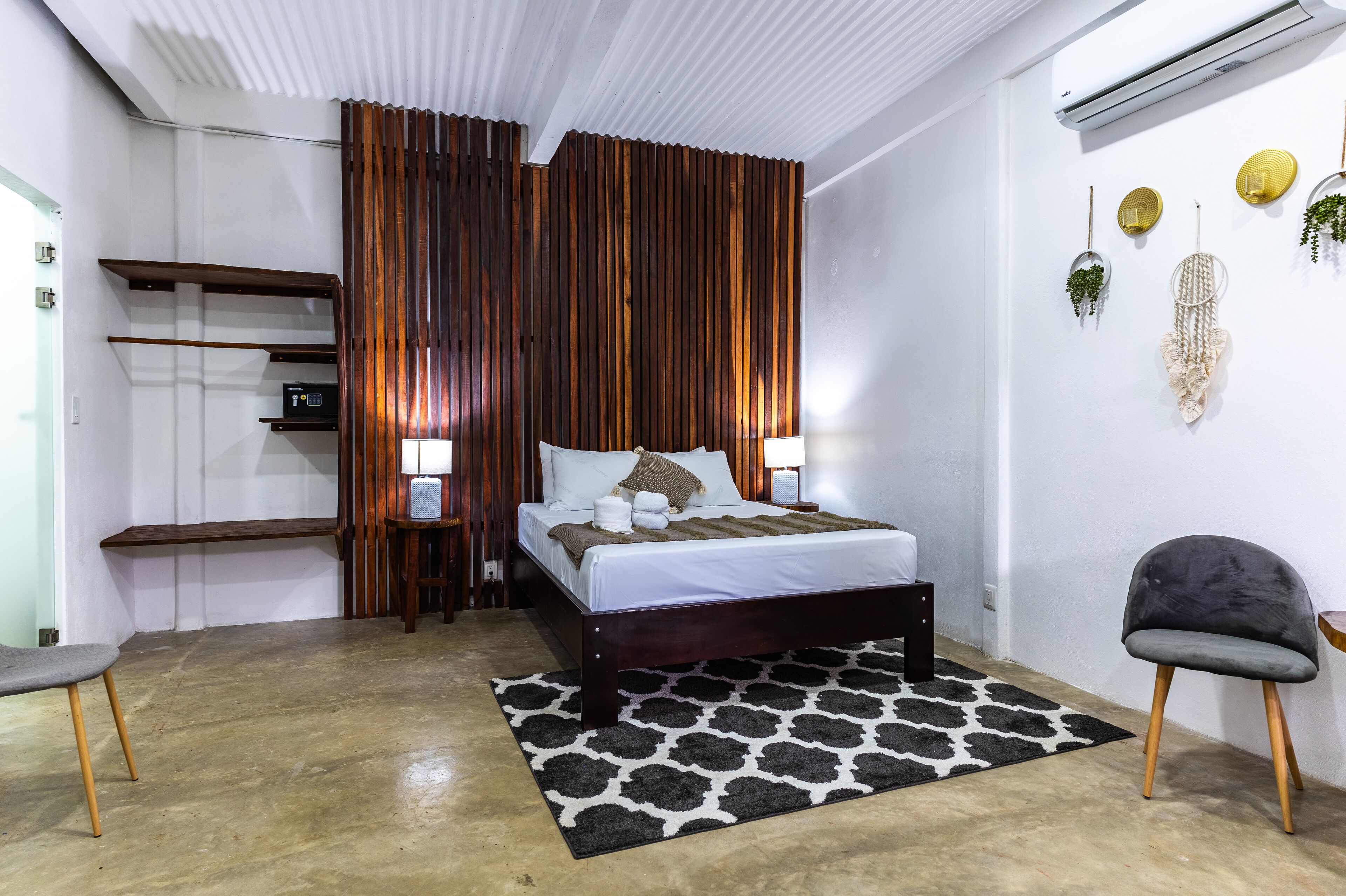 A modern bedroom with a wooden bed, bedside lamps, a black and white patterned rug, and a grey chair.