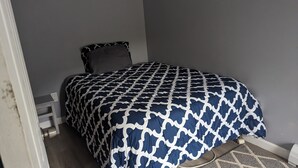 A bedroom with a bed, grey walls, and a patterned bedspread.