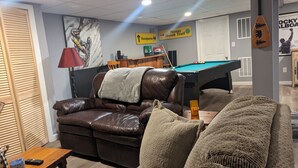A living room with a pool table, a leather sofa, and a billiards cue rack.