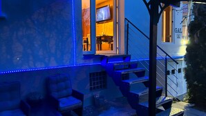 An outdoor seating area with blue LED lights, a staircase, and a view of a building with a 'GAL' sign.