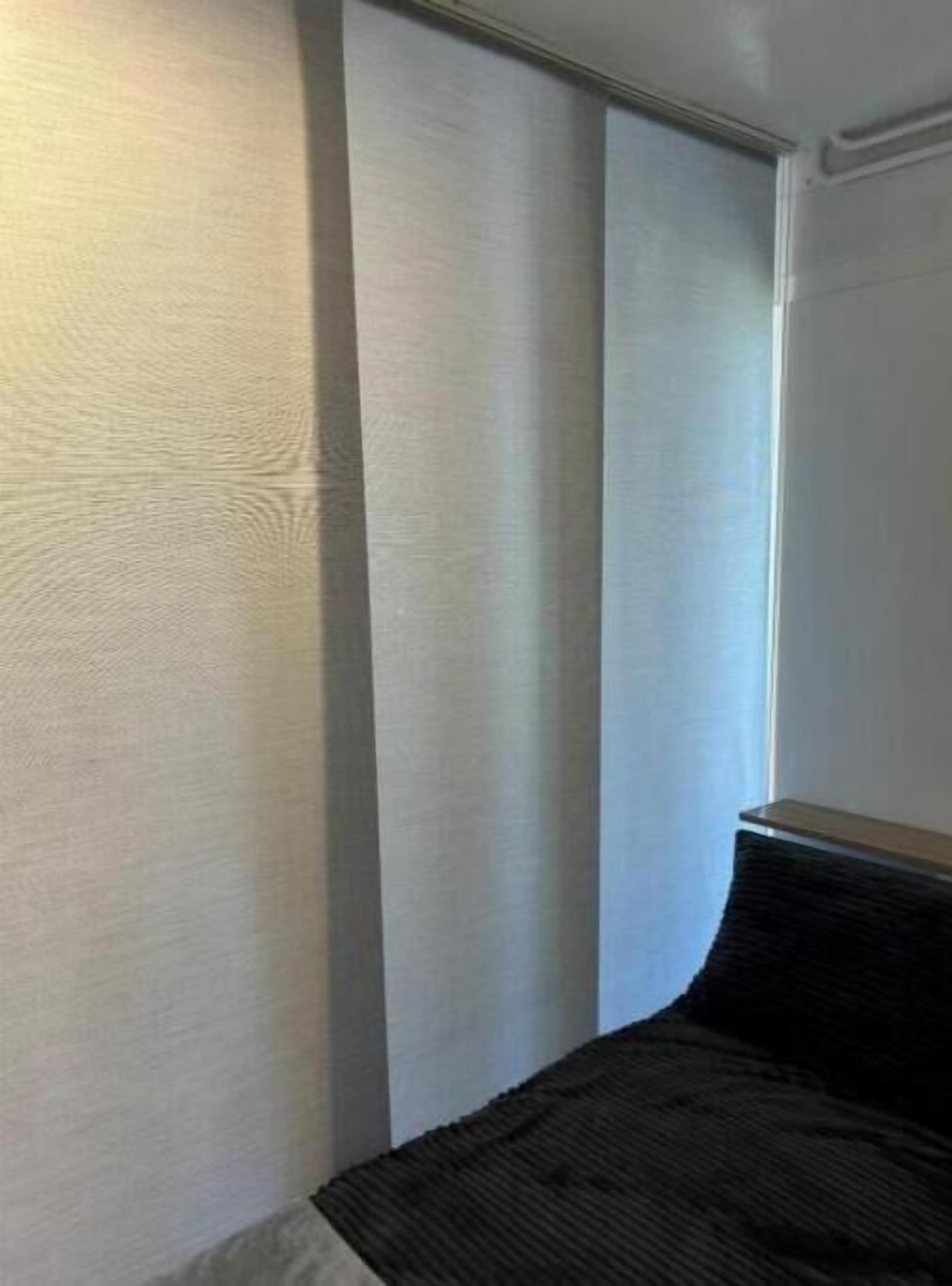 A room with a bed, a window with blinds, and a wall with a textured surface.