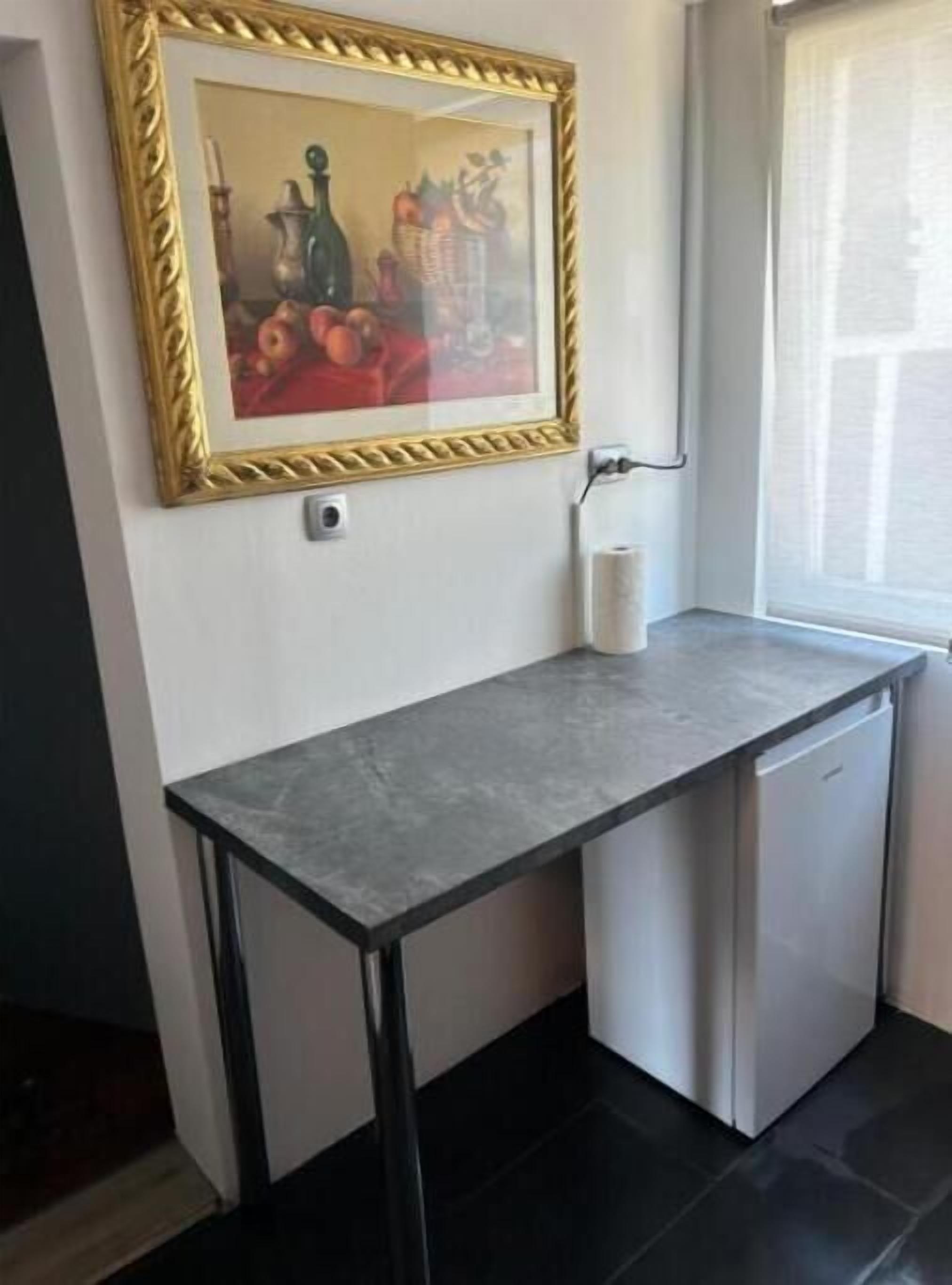 A small kitchenette with a countertop, a refrigerator, and a wall-mounted sink.