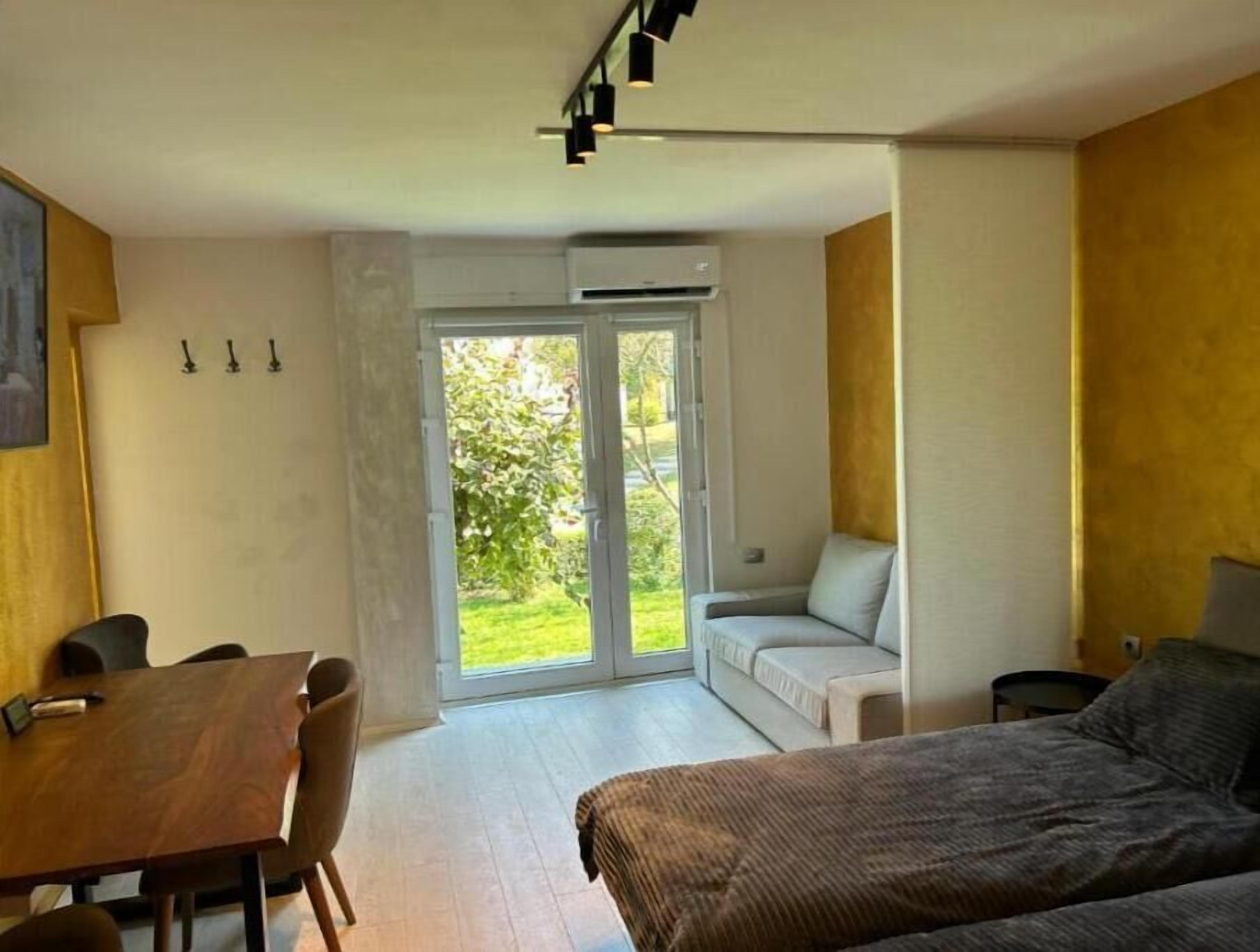 Quarto moderno com mesa de jantar, cadeiras, sofá e cama. Possui uma porta de vidro deslizante que dá para um jardim.