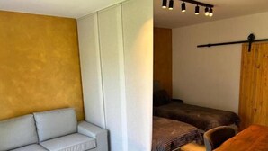 A room with a sofa, a bed with a striped blanket, a wooden table, and a ceiling light fixture.