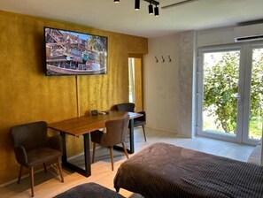 A modern room with a bed, a desk, two chairs, a television mounted on the wall, and a large window with a view of greenery. - APARTMENT GAL (Novo mesto)