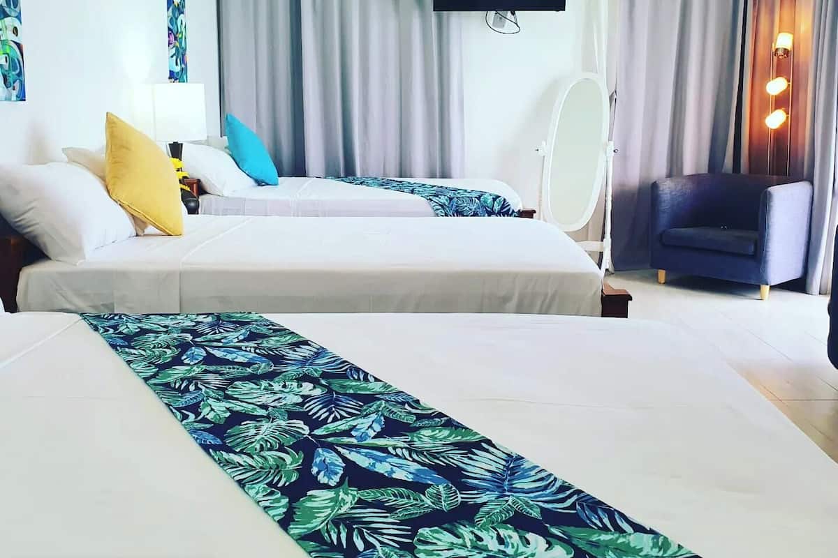 A hotel room with two beds, a TV, a mirror, a chair, and a window with curtains.