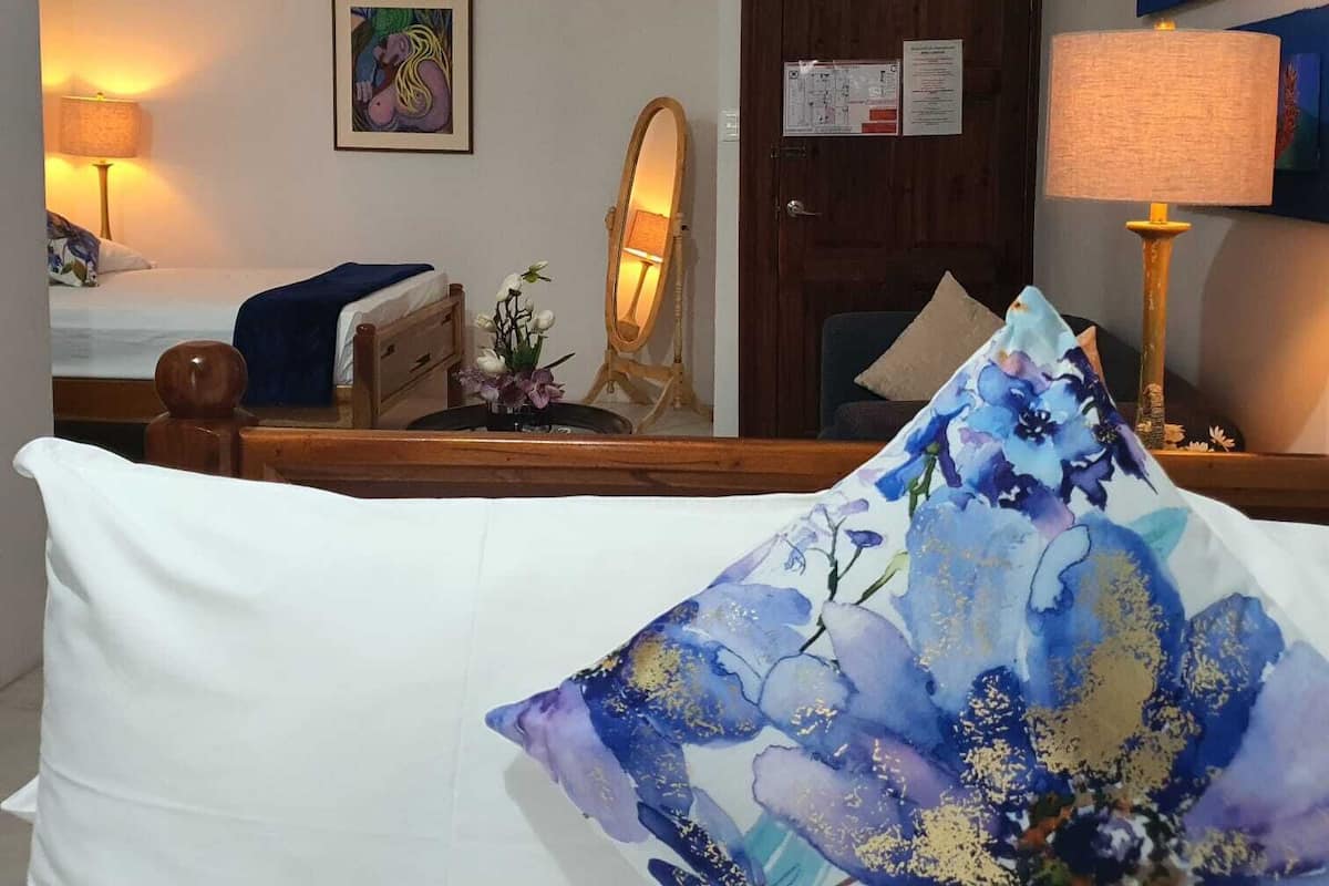 A hotel room with a bed, a ceiling fan, a door with a notice, a mirror, and a lamp.