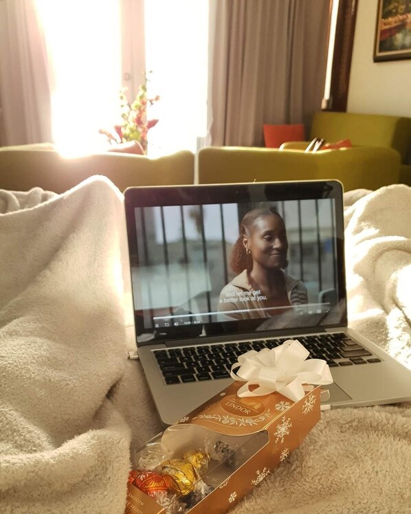 A laptop on a bed with a gift box and chocolates.