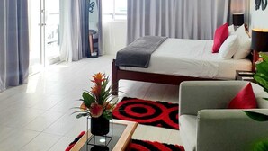 A hotel room with a bed, a desk, a chair, a plant, and a ceiling fan. - Merci Buccoo (Scarborough)